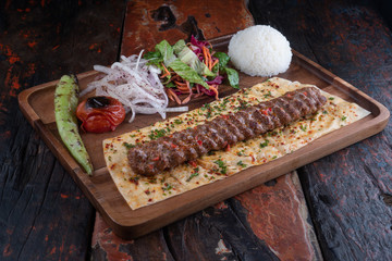 Turkish lula lamb or beef kebab with rice and vegetables isolated on rustic wooden table