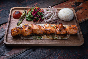 Turkish chicken sis kebab with rice and vegetables isolated on rustic wooden table