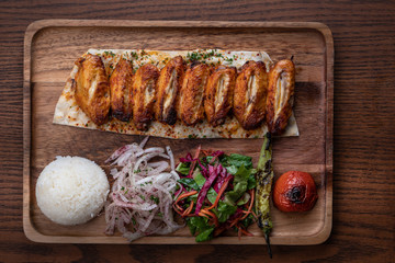 Turkish chicken wings kebab with rice and vegetables isolated on wooden table