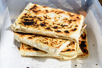 Traditional Turkish dish called gozleme, made of flat bread stuffed with meat or cheese and baked on sheet iron, displayed on a white table, available for sale at a street food market
