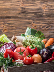 Fresh multi-colored vegetables in wooden crate. Wooden background.