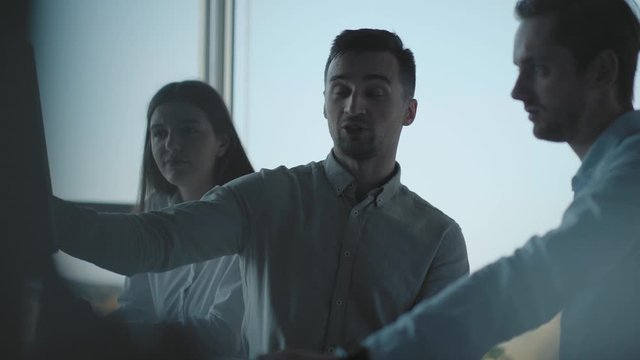Creative business team meeting in modern start up office. Male team leader pointing at screen, discussing diverse people group teamwork. Three handsome people in the office in front of the computer.