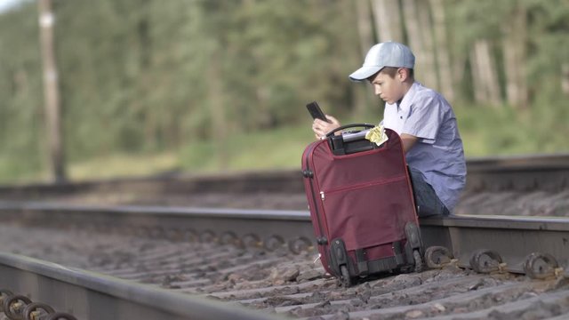 sad and angry traveler boy reads messages on the phone sits on the railway