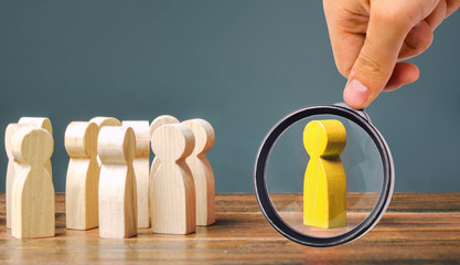 A magnifying glass looks at a yellow figurine of a man stands aside from the crowd of people....