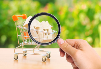 A magnifying glass looks at a wooden house in a trading cart on nature background. The concept of...