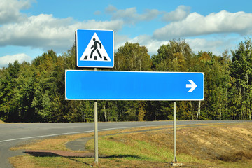 Road signs direction indicator and pedestrian crossing on a road bend, against the sky and forest...