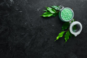 Green sea salt in a glass jar On a black stone background. Spa treatments. Top view. Free space for your text.