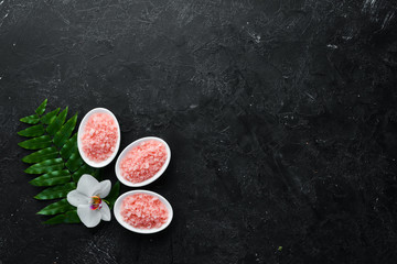 Pink fragrant sea salt in a bowl. On a black stone background. Spa treatments. Top view. Free space...