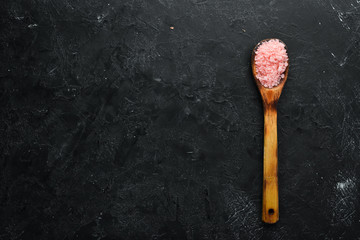 Fototapeta na wymiar Pink fragrant sea salt in spoon. On a black stone background. Spa treatments. Top view. Free space for your text.
