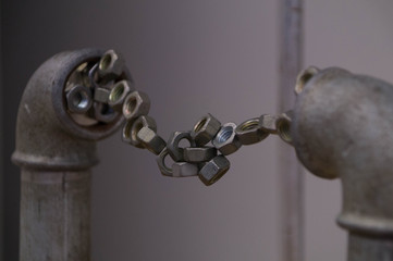 A chain of metal nuts stretches from pipe to pipe using magnetism