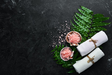 Pink sea salt with towels and tropical leaf. On a black stone background. Spa treatments. Top view. Free space for your text.