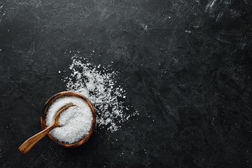 Salt in a wooden spoon. Sea salt. On a black stone background. Spa treatments. Top view. Free space...