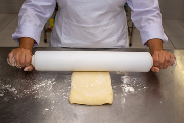 Chef hands rolling the dough with the rolling pin. Making puff pastry on a stainless steal table. First step, dough and the butter on the table.Close up. pastry chef. how to make.