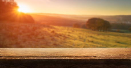 A wooden table top product display with a blurred background scene of golden sunset fields.