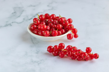 Red currants on a white plate on a marble background.