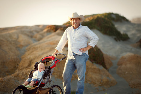 Portrait of a man in a cowboy had standing next to his young son in a stroller.