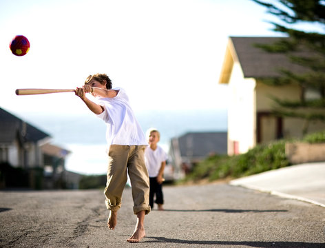 Two brothers playing baseball together on a street.