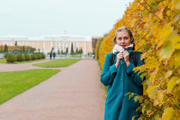 Autumn and walks. A young woman is wrapped in a coat, posing near a vegetable fence, with yellow leaves. Copy space. Horisontal orientation