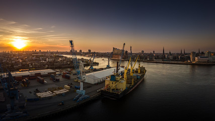 Fototapeta na wymiar Die Elbphilharmonie im Hafen von Hamburg bei Sonnenuntergang mit Containerschiff im Vordergrund