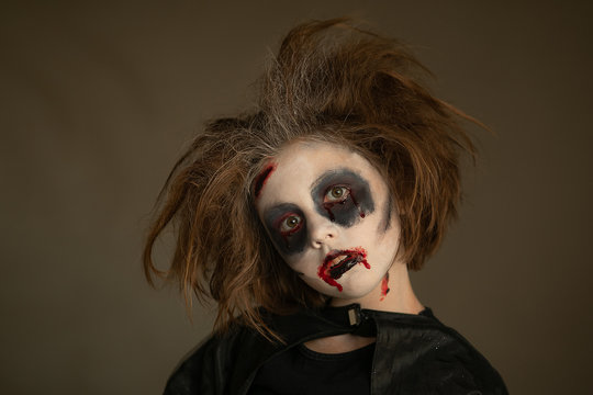 A child in a carnival costume with a scary face painting on Halloween. Black background.