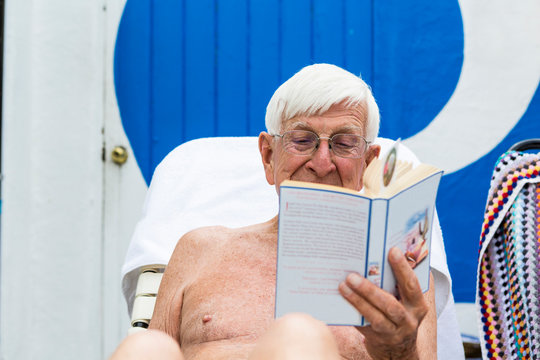 Shirtless senior man reading book outdoors