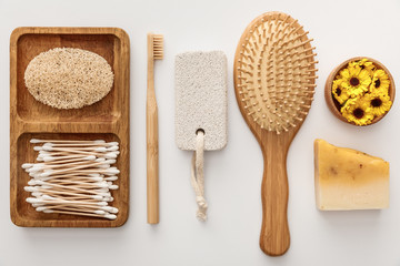 flat lay with wooden dish with cotton swabs and loofah near toothbrush, hairbrush, piece of soap,...