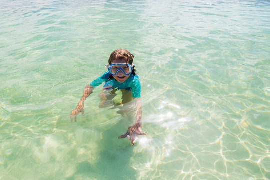 5 year old boy in the water holding a star fish, Grand Cayman Island