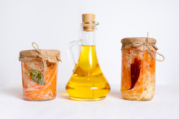 three jars of sauerkraut and carrots in its own juice with spices and a bottle of oil, white wooden table. traditional home-made, fermented dish of Russia and Germany