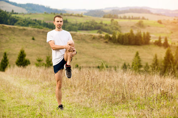 Fototapeta na wymiar Runner man stretching legs before cross country trail run. Fit male runner exercise training outdoors in beautiful autumn mountain nature landscape