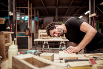 Male carpenter looking at wood while working at workbench in workshop