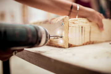 Cropped hands of female carpenter drilling wood at workbench in workshop