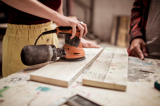 Midsection of female carpenter sanding wood while standing by male colleague at desk