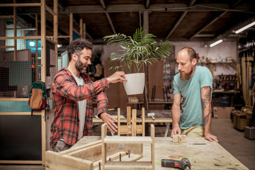Male carpenter showing wooden plant pot holder to colleague while discussing at workbench in workshop