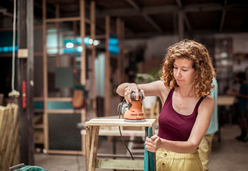 Female carpenter with redhead sanding wooden table in workshop