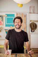 Smiling male carpenter with disposable cup standing at desk in workshop