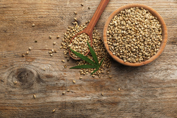 Organic hemp seeds and leaf on wooden background, flat lay. Space for text