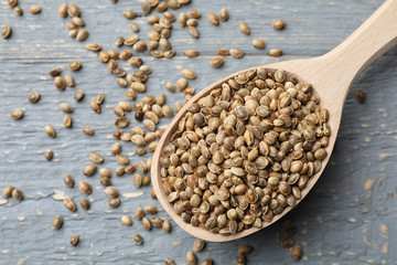 Organic hemp seeds in spoon on grey wooden table, top view
