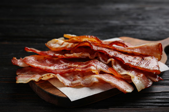 Slices of tasty fried bacon on black wooden table, closeup