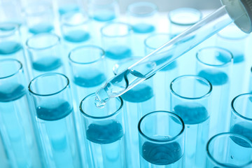 Dropping sample into test tube with light blue liquid, closeup