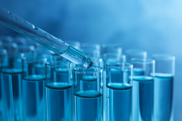 Dropping sample into test tube with liquid on blue background, closeup