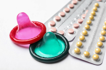 Obraz na płótnie Canvas Condoms and birth control pills on white background, closeup. Safe sex concept