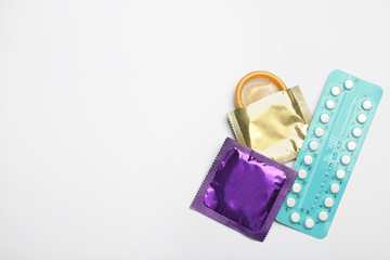 Condoms and birth control pills on light grey background, flat lay with space for text. Safe sex...