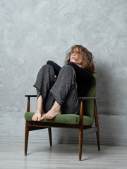 Girl with wild messy hair sitting on armchair with legs