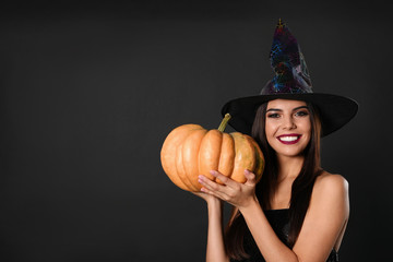 Beautiful woman wearing witch costume with pumpkin for Halloween party on black background, space...