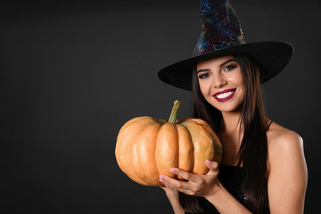 Beautiful woman wearing witch costume with pumpkin for Halloween party on black background, space...