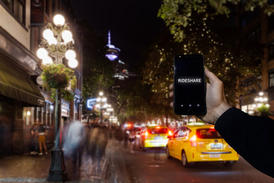 A cell phone with the the words rideshare on the screen superimposed over a view of a city street in Downtown Vancouver.