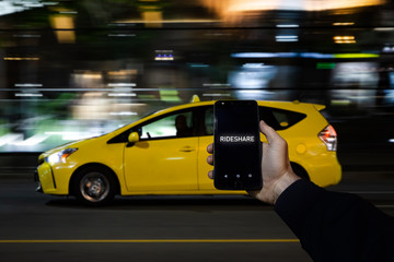 A cell phone with the the words rideshare on the screen on in front of a yellow taxi in the background. - obrazy, fototapety, plakaty