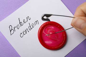 Woman piercing condom with pin on purple background, closeup. Safe sex