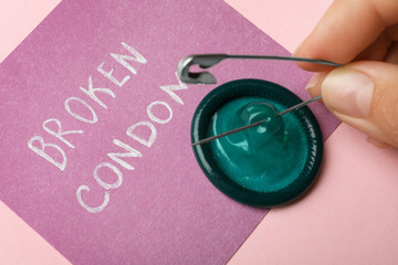 Woman piercing condom with pin on pink background, closeup. Safe sex