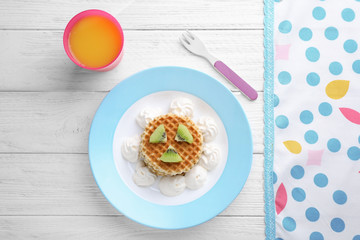 Tasty waffles served with whipped cream and juice on white wooden table, flat lay. Creative idea for kids breakfast